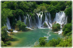 Einige Wasserfälle, die in einem Fluss münden und von unberührter Natur umgeben sind.